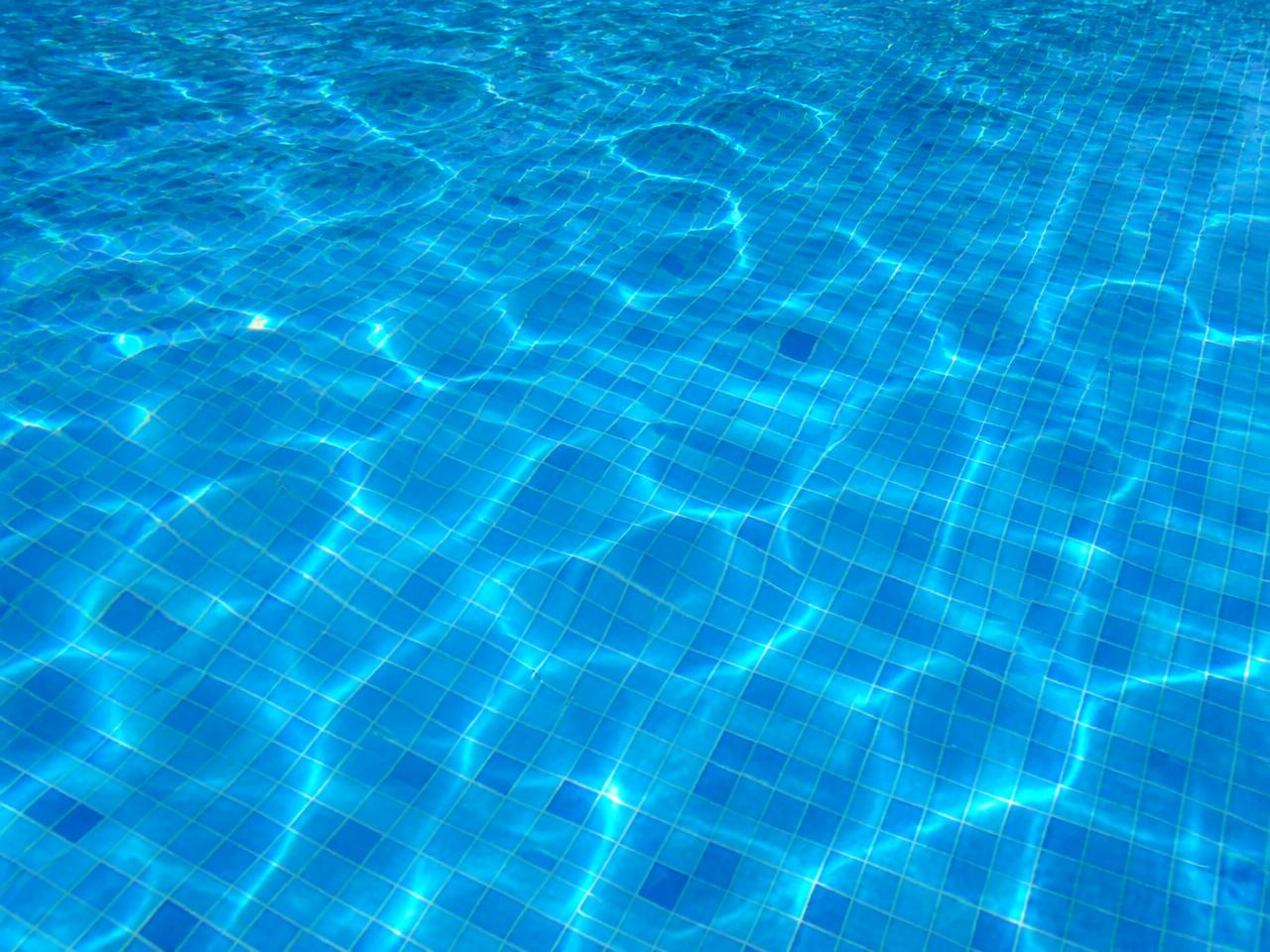 Superfície de água de piscina cristalina com reflexos de sol sobre pastilhas azuis